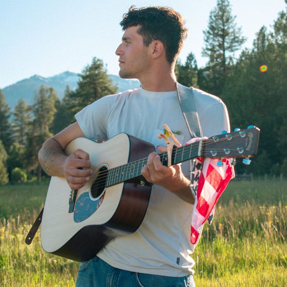 Anthony playing his acoustic guitar in a mountain meadow